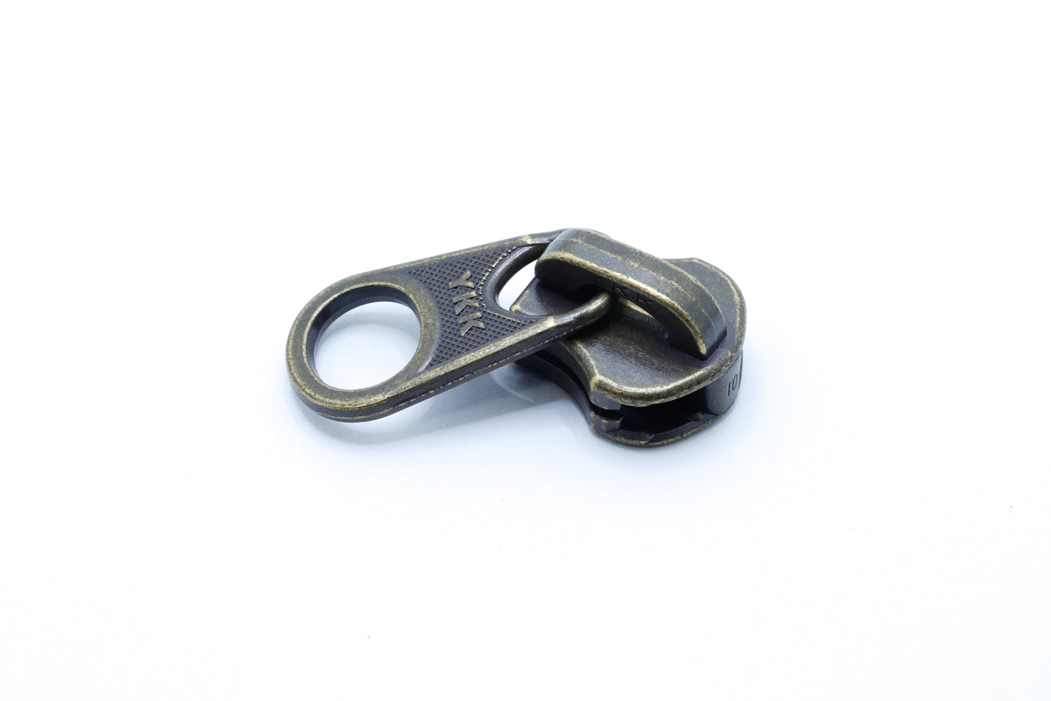 One antique brass YKK metal zipper slider with large circular pull tabs, displayed on a white background, showing size difference and vintage finish.