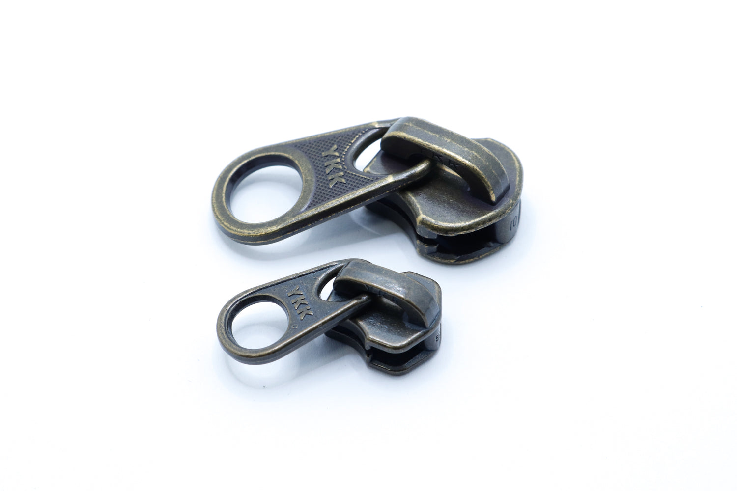 Two antique brass YKK metal zipper sliders with large circular pull tabs, displayed on a white background, showing size difference and vintage finish.