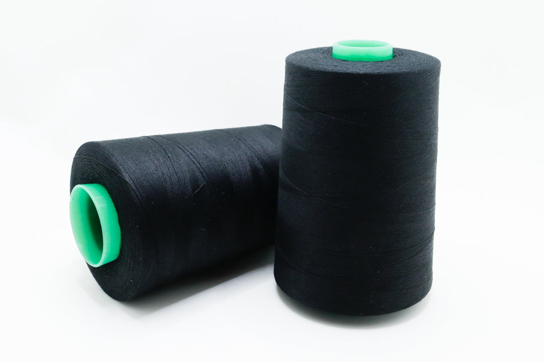 Two black spools of thread with green ends on a white background