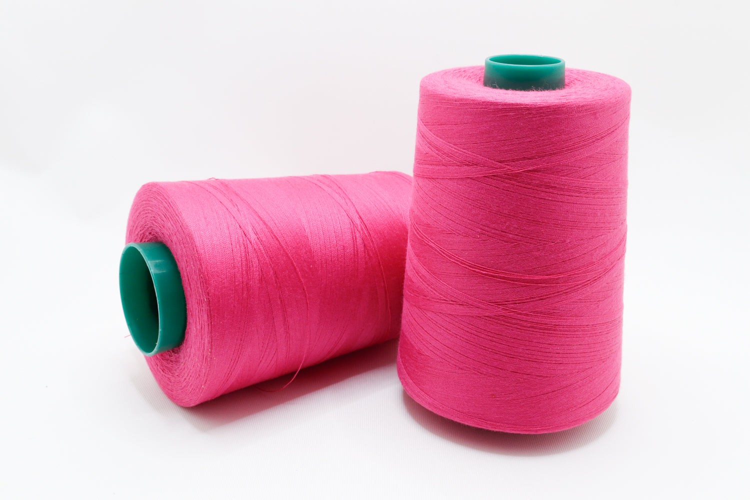 Two pink spools of thread on a white background used for sewing