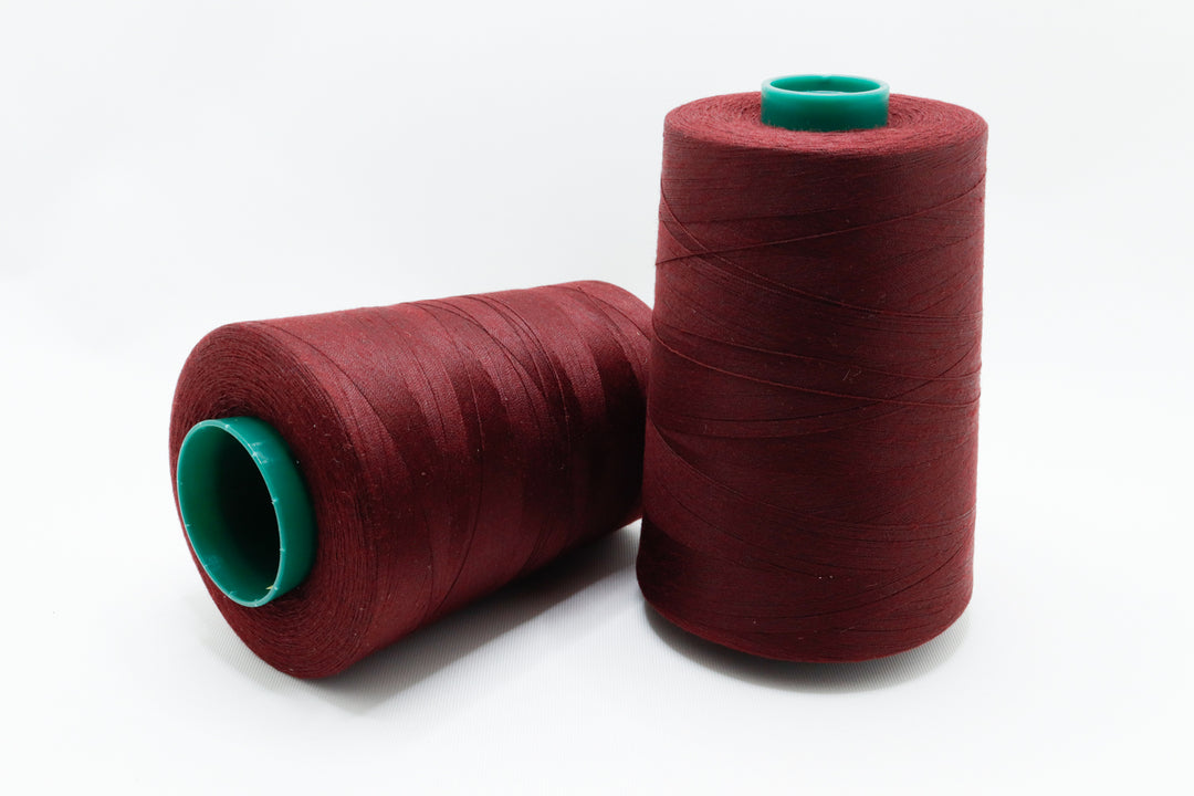 Two spools of red thread with green ends on a white background