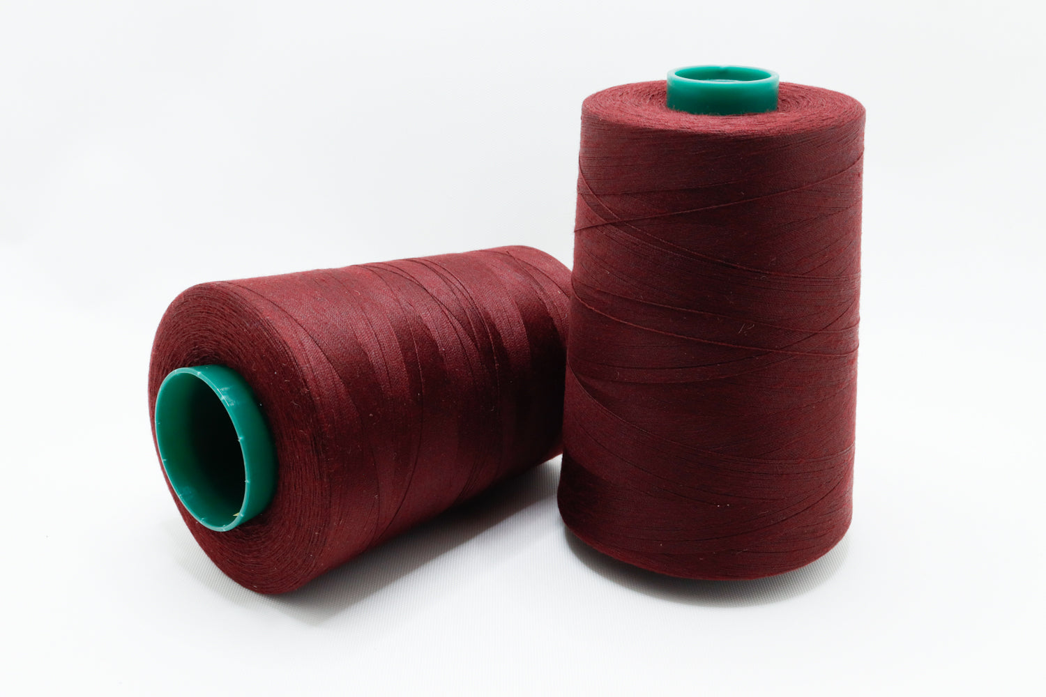 Two spools of red thread with green ends on a white background