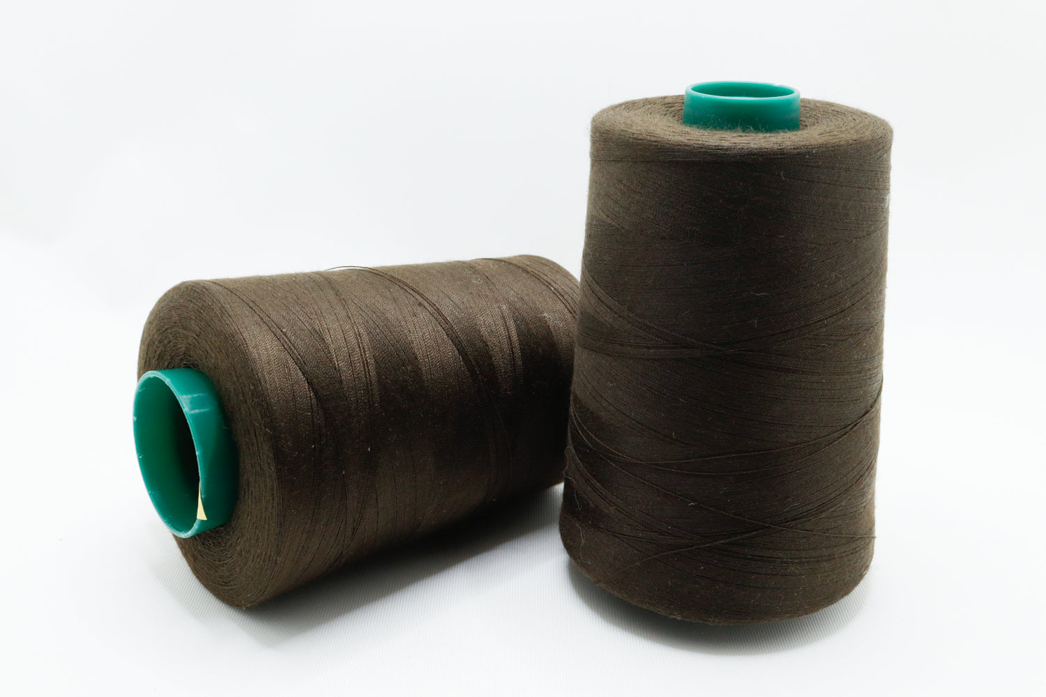 Two spools of brown thread with green ends on a white background