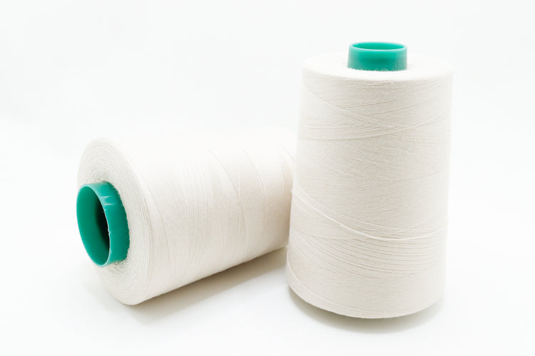 Two spools of white thread with green ends on a white background