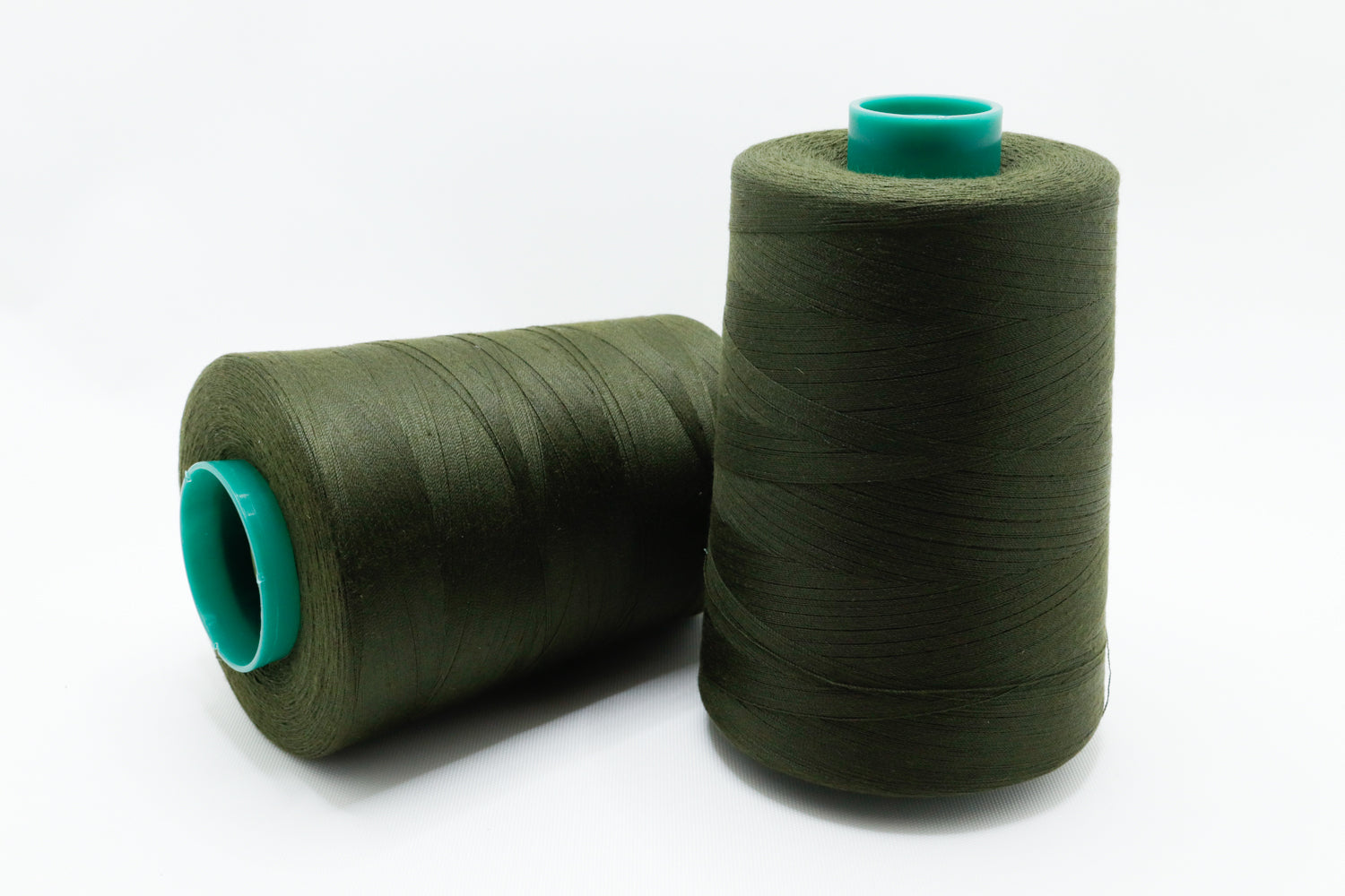 Two spools of green thread with teal ends on a white background