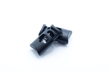 Black plastic cord lock toggle shown from the side, used to cinch drawstrings on packs and stuff sacks